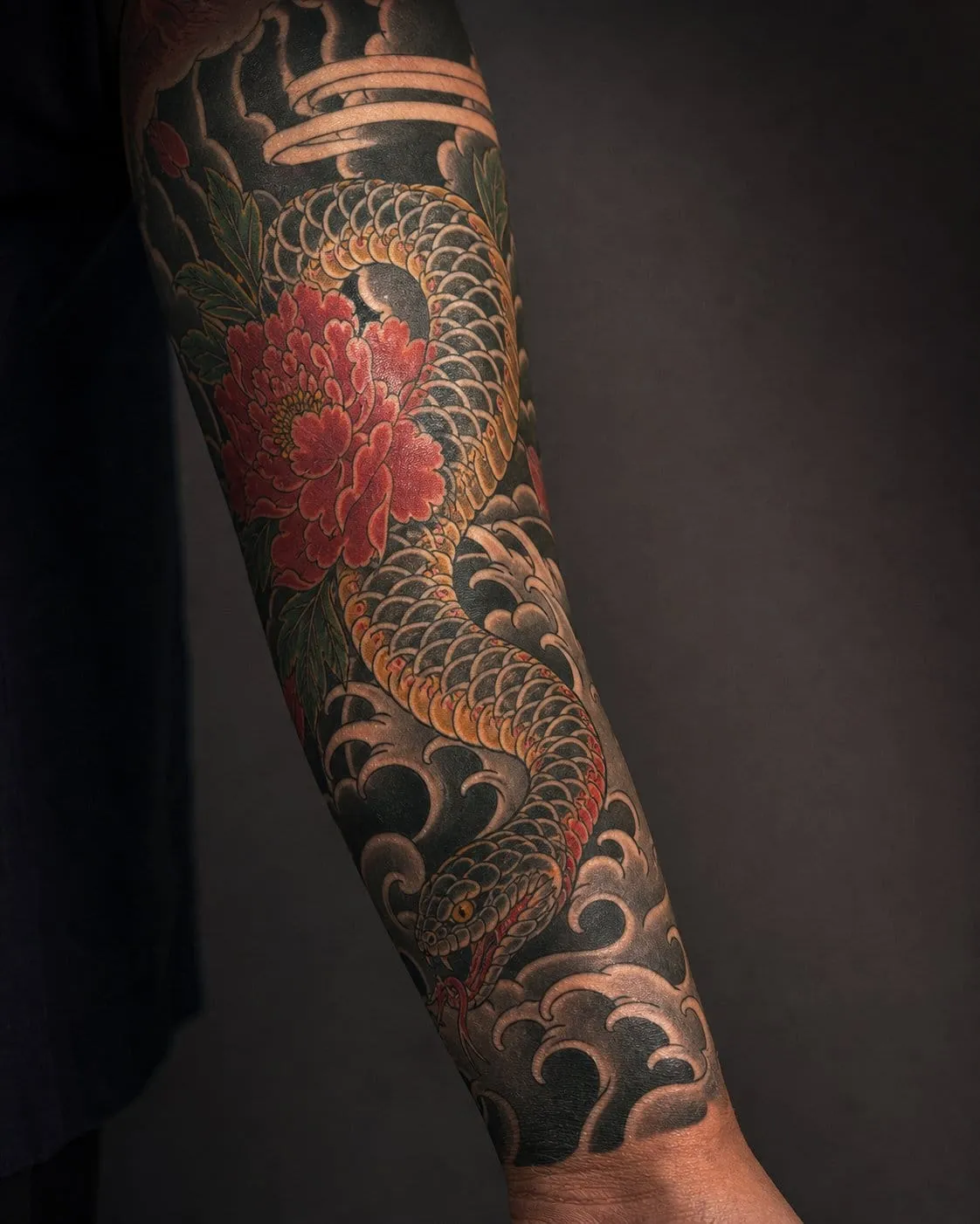Japanese hebi snake tattoo with a peony and wave background flowing down an arm.