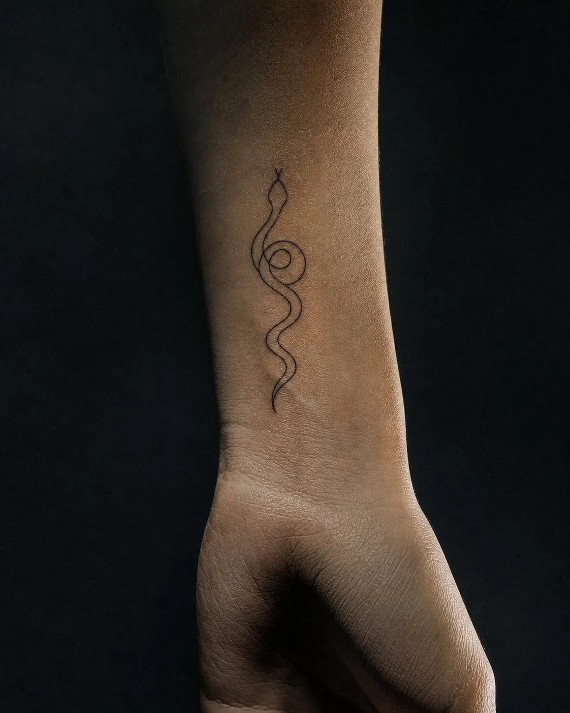 Minimalist single-line snake tattoo curling on a wrist, almost entirely negative space.